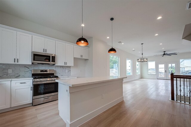 kitchen with stainless steel appliances, hanging light fixtures, white cabinets, and light hardwood / wood-style floors