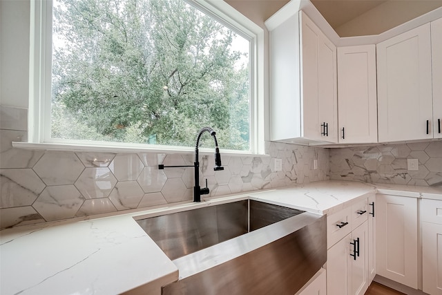 kitchen featuring light stone counters, white cabinetry, sink, and tasteful backsplash