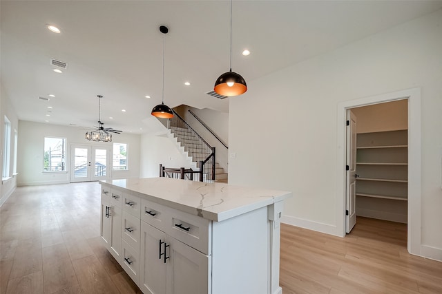 kitchen with light stone countertops, hanging light fixtures, light hardwood / wood-style flooring, and white cabinets