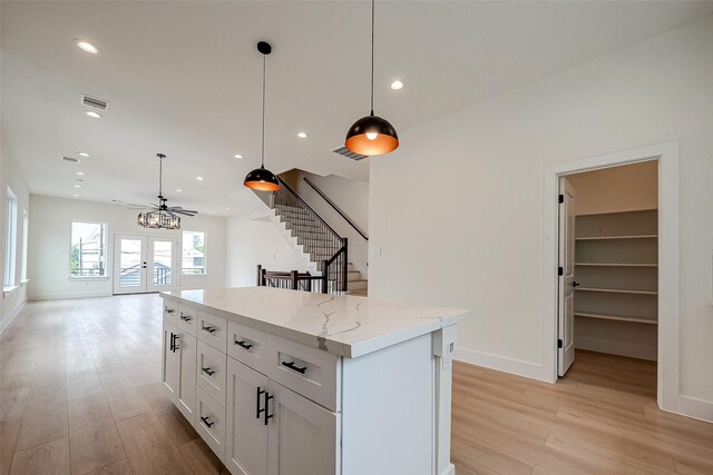 kitchen featuring light stone countertops, a kitchen island, white cabinetry, and pendant lighting