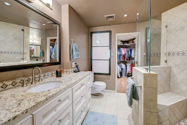 bathroom with tiled shower, tile patterned flooring, toilet, and vanity