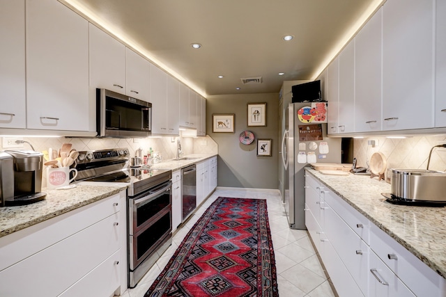 kitchen with backsplash, appliances with stainless steel finishes, white cabinets, and light tile patterned flooring