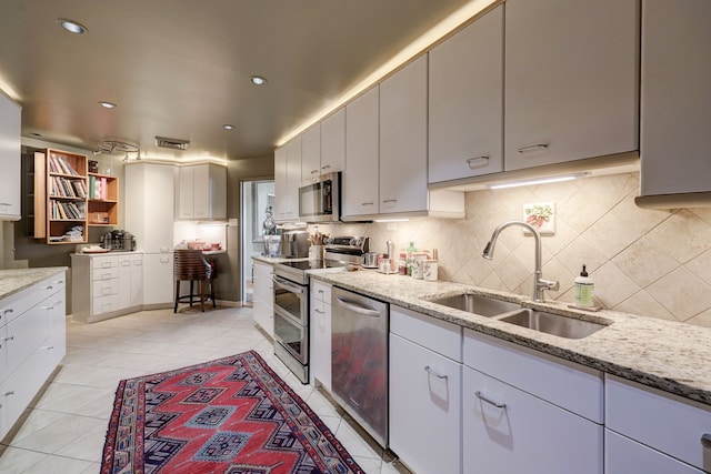 kitchen with light tile patterned floors, backsplash, stainless steel appliances, sink, and light stone counters