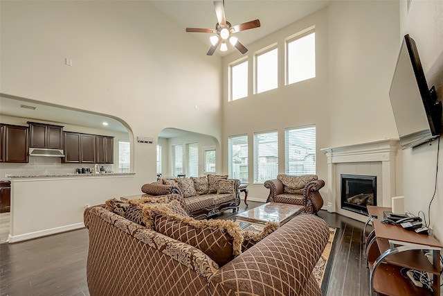 living room with dark wood-type flooring, ceiling fan, high vaulted ceiling, and a fireplace