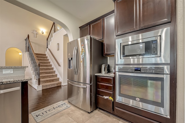 kitchen with appliances with stainless steel finishes, light stone countertops, dark brown cabinetry, and light hardwood / wood-style flooring