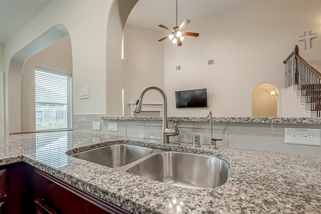 kitchen with high vaulted ceiling, ceiling fan, light stone counters, and sink