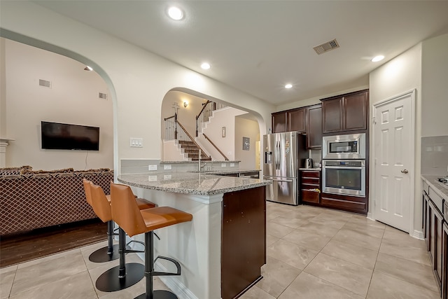 kitchen with appliances with stainless steel finishes, light stone counters, sink, kitchen peninsula, and dark brown cabinetry