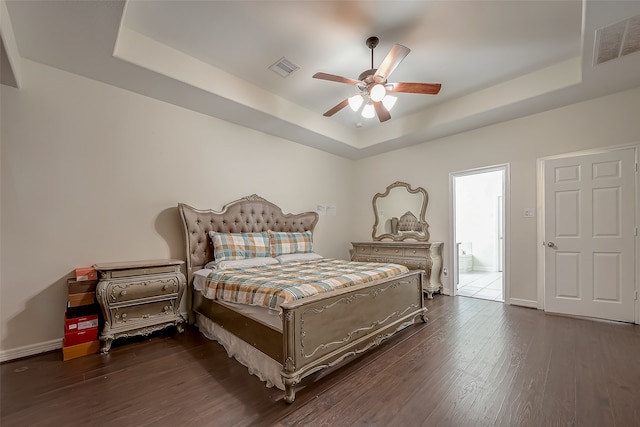 bedroom featuring a tray ceiling, dark hardwood / wood-style flooring, ensuite bathroom, and ceiling fan