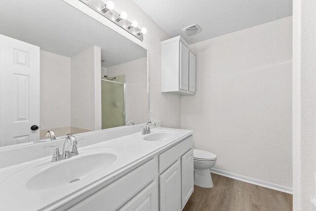 full bath featuring double vanity, a sink, a shower stall, and wood finished floors