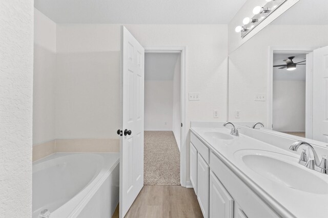 full bath featuring a garden tub, double vanity, wood finished floors, and a sink