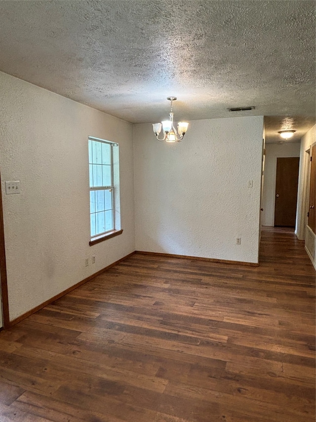 spare room with a textured ceiling, dark wood-type flooring, and a chandelier