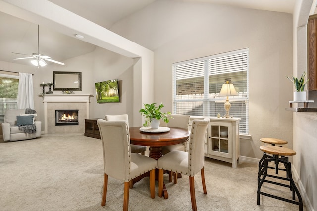 carpeted dining room featuring high vaulted ceiling, a tiled fireplace, ceiling fan, and a healthy amount of sunlight