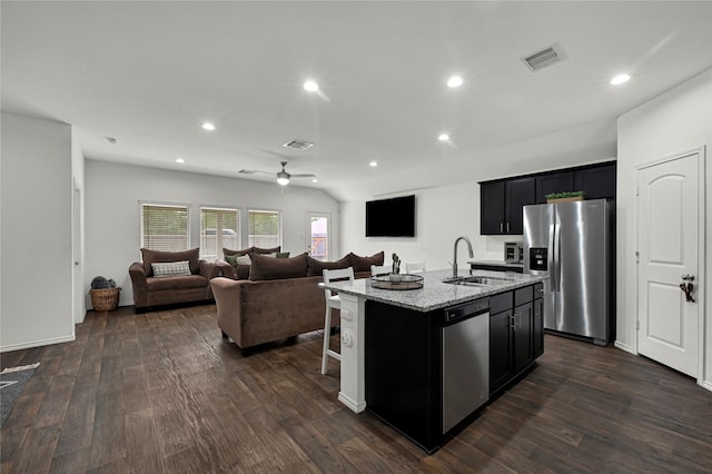 kitchen featuring stainless steel appliances, light stone counters, an island with sink, sink, and dark wood-type flooring