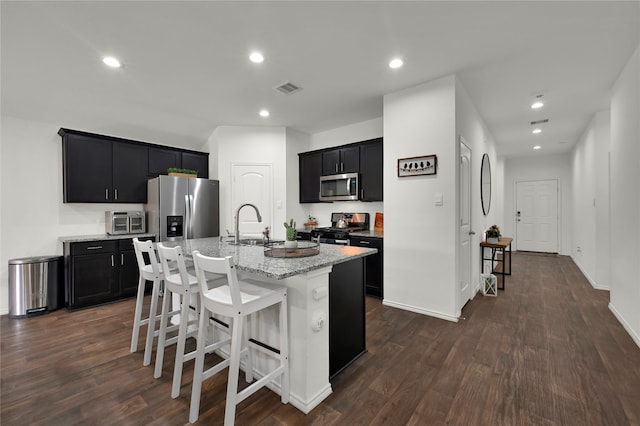 kitchen featuring a kitchen breakfast bar, dark hardwood / wood-style flooring, an island with sink, light stone countertops, and appliances with stainless steel finishes