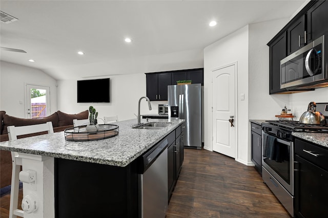 kitchen with dark hardwood / wood-style flooring, appliances with stainless steel finishes, an island with sink, sink, and light stone counters