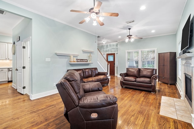 living room with ceiling fan, light hardwood / wood-style floors, ornamental molding, and a tiled fireplace