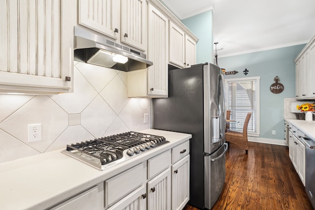 kitchen with backsplash, white cabinets, ornamental molding, appliances with stainless steel finishes, and dark hardwood / wood-style flooring