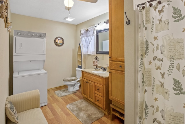 bathroom featuring toilet, hardwood / wood-style floors, vanity, stacked washer and clothes dryer, and ceiling fan