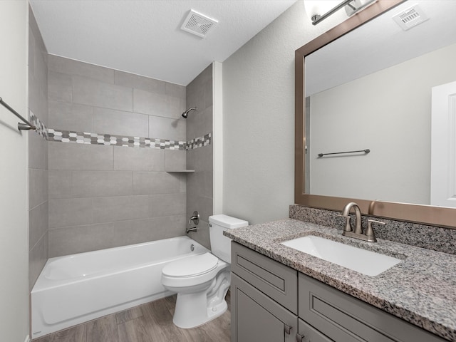 full bathroom with hardwood / wood-style floors, toilet, tiled shower / bath combo, vanity, and a textured ceiling