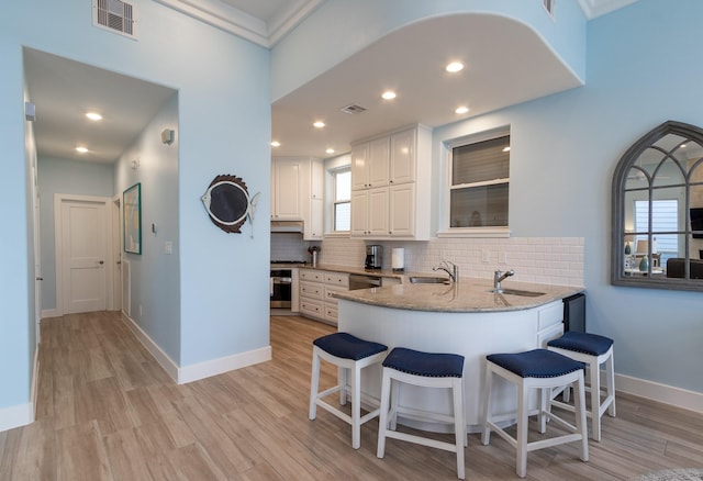 kitchen featuring sink, appliances with stainless steel finishes, white cabinetry, light stone counters, and kitchen peninsula