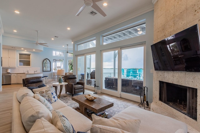 living room with light hardwood / wood-style floors, ceiling fan, ornamental molding, and a premium fireplace