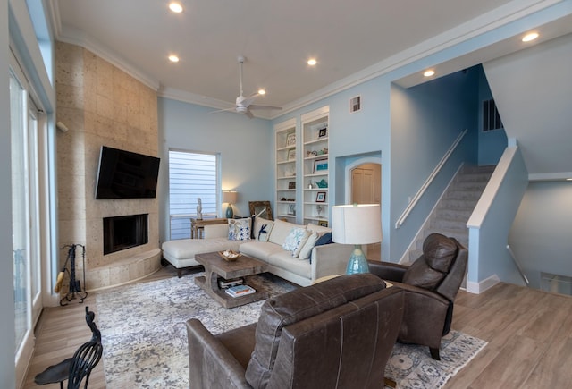 living room with ornamental molding, ceiling fan, light hardwood / wood-style flooring, built in features, and a fireplace