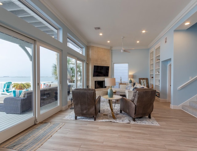 living room with built in shelves, ceiling fan, a fireplace, and crown molding