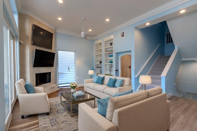 living room with light wood-type flooring, built in shelves, a large fireplace, and crown molding