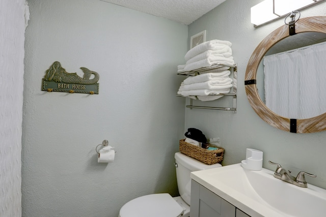 bathroom with a textured ceiling, vanity, and toilet