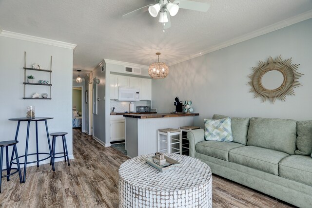 living room featuring ceiling fan with notable chandelier, crown molding, and wood-type flooring