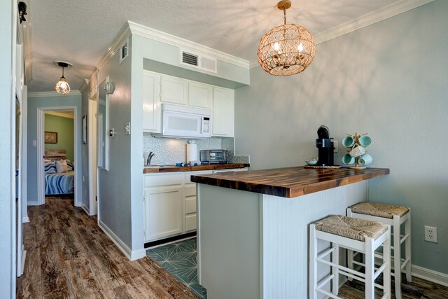 kitchen with a breakfast bar area, dark hardwood / wood-style floors, pendant lighting, wood counters, and white cabinetry