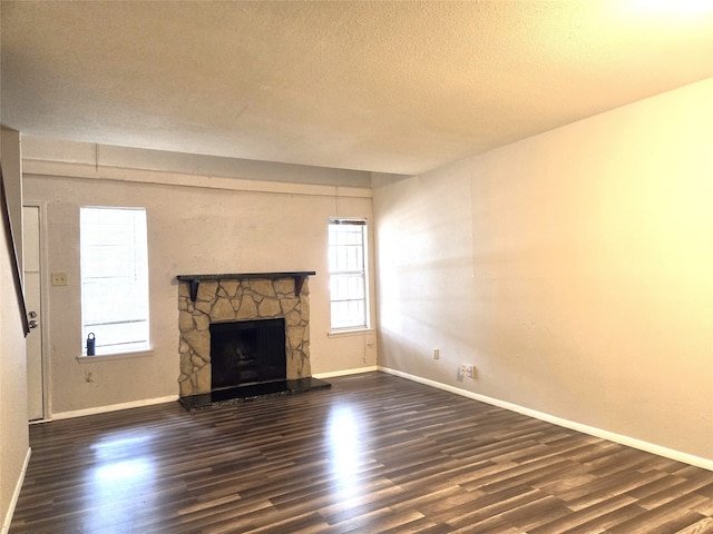 unfurnished living room featuring a textured ceiling, dark wood-type flooring, and a stone fireplace