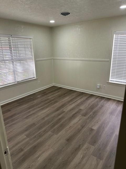 unfurnished room with a wealth of natural light, visible vents, a textured ceiling, dark wood finished floors, and wainscoting