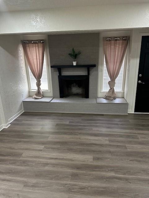 unfurnished living room featuring a fireplace, baseboards, a textured wall, and wood finished floors