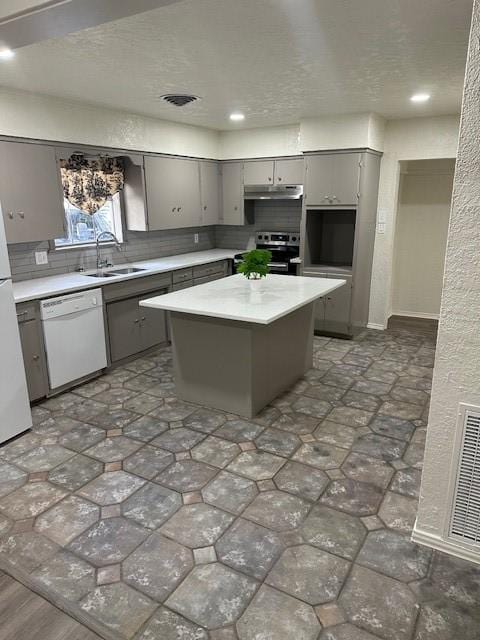 kitchen with white appliances, gray cabinets, a sink, under cabinet range hood, and tasteful backsplash