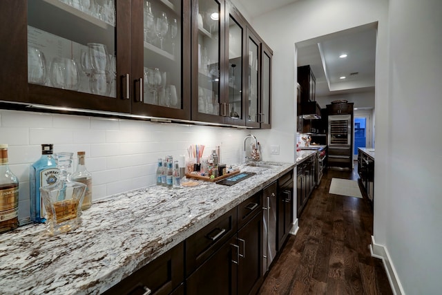 kitchen featuring dark hardwood / wood-style flooring, sink, light stone countertops, decorative backsplash, and dark brown cabinetry