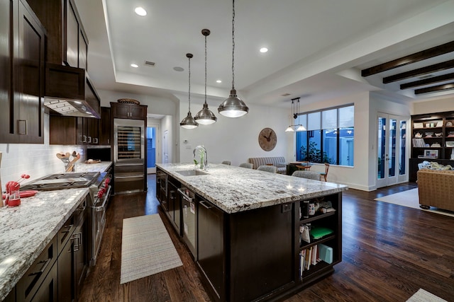 kitchen featuring dark hardwood / wood-style flooring, light stone countertops, an island with sink, and dark brown cabinetry