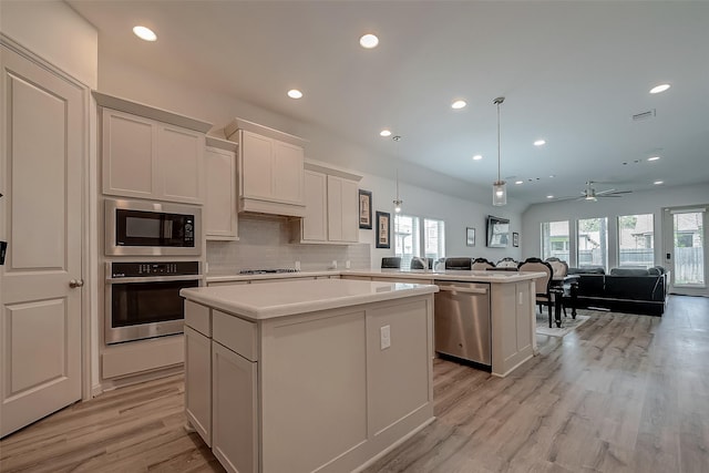 kitchen featuring stainless steel appliances, a kitchen island, open floor plan, light countertops, and tasteful backsplash