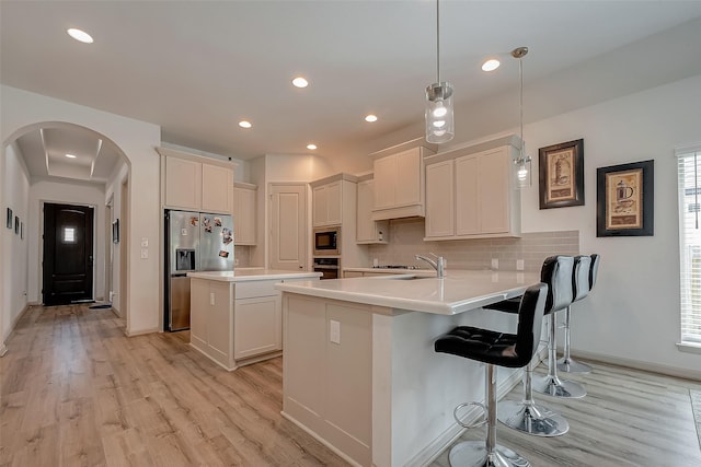 kitchen featuring arched walkways, stainless steel appliances, tasteful backsplash, a sink, and a peninsula