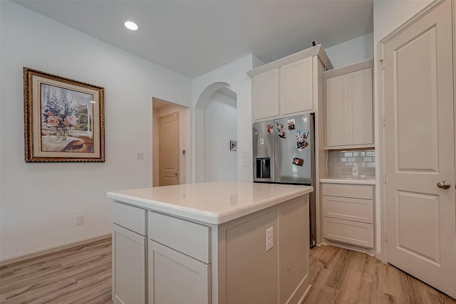 kitchen with arched walkways, a center island, light wood finished floors, light countertops, and backsplash