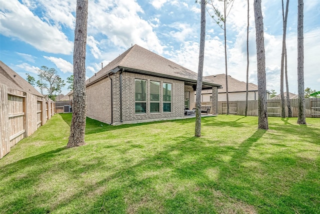 back of house with brick siding, a yard, a fenced backyard, and roof with shingles