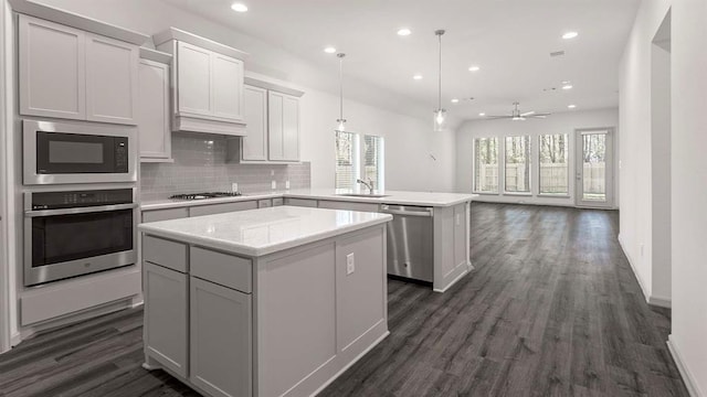 kitchen featuring stainless steel appliances, a peninsula, a sink, a kitchen island, and decorative backsplash