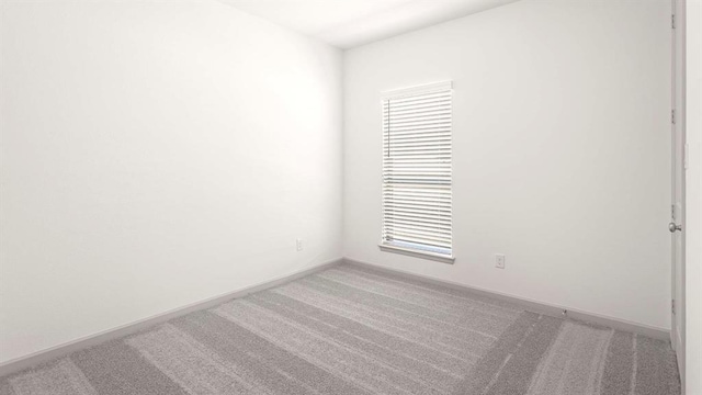 spare room featuring light carpet and baseboards