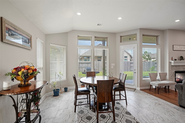 dining room featuring lofted ceiling, a healthy amount of sunlight, a high end fireplace, and light wood-type flooring