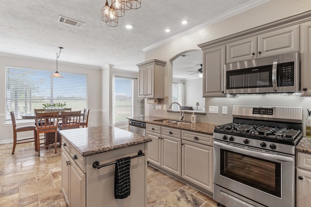 kitchen featuring stone tile floors, stainless steel appliances, a sink, visible vents, and crown molding