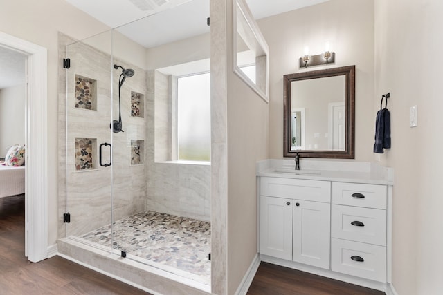 ensuite bathroom featuring visible vents, a shower stall, vanity, wood finished floors, and baseboards