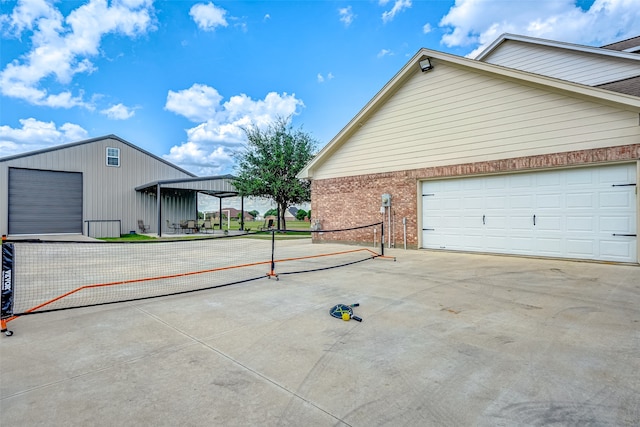 view of side of home with a tennis court, concrete driveway, and brick siding