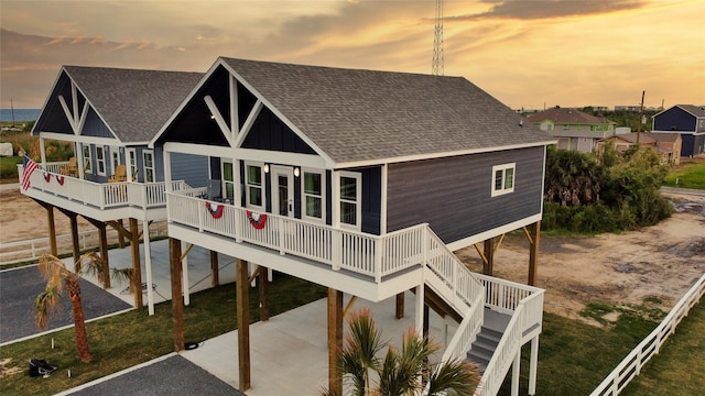 rear view of house with covered porch, a shingled roof, stairway, and board and batten siding