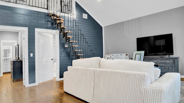 living room with high vaulted ceiling, wood walls, baseboards, and wood finished floors