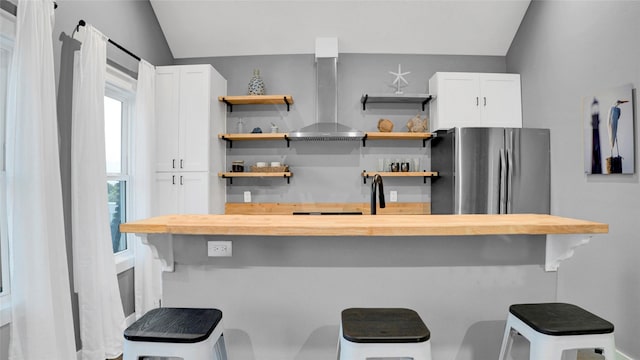 kitchen featuring open shelves, wall chimney range hood, butcher block countertops, and freestanding refrigerator